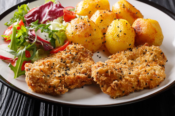 Delicious fried steaks in sesame breading served with new potatoes and fresh salad close-up on a...