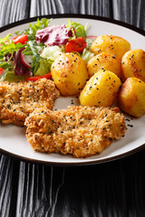 Pork cutlet in sesame breading with new potatoes and fresh salad close-up on a plate. vertical