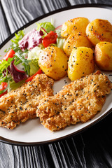 Fried pork steak in sesame breaded with new potatoes and salad closeup on a plate. vertical