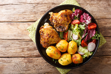 full dinner of chicken thighs with new potatoes and fresh salad close-up on a plate. horizontal top view