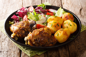 Portion of chicken thighs with new potatoes and fresh salad close-up on a plate. horizontal