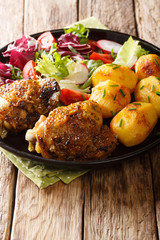 Delicious chicken thighs served with young potatoes and fresh salad close-up on a plate. vertical