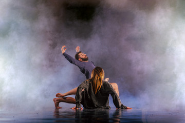 Shoeless dance couple performing multiple unique dance moves in front of a black background surrounded by a lot of smoke.