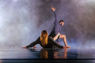 Shoeless dance couple performing multiple unique dance moves in front of a black background surrounded by a lot of smoke.