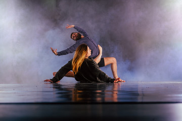 Shoeless dance couple performing multiple unique dance moves in front of a black background surrounded by a lot of smoke.