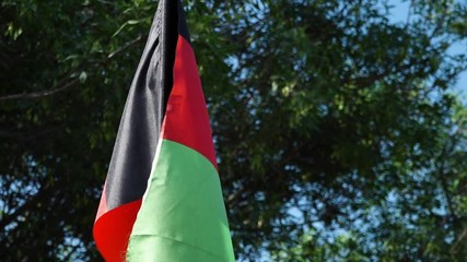A hand held, panning, extreme close up shot of the flag of Afghanistan, while it dances in the wind of the day.