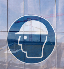Symbol on a transparent tarpaulin, through which parts of the jobsite are seen, as an indication of safety on a construction site. You can see that you should wear a hard hat.