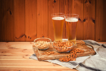 Two glasses of light  beer with salted pretzels and peanuts on  wooden table.