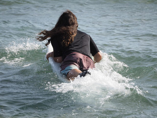 adult surfer with long hair walks into the ocean holding a white surfboard. back view.