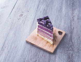 A slice of homemade purple ombre layer cake, vanilla layer cake with violet and withe butter cream frosting, on the wooden plate that on the grey wooden table with copy space.