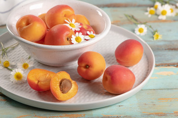 Delicious ripe apricots in a bowl on the wooden table. Close-up with apricots and daisy flowers