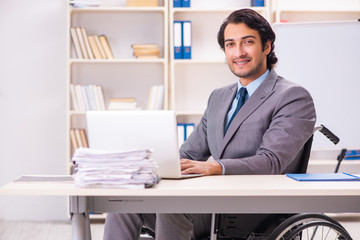 Young handsome employee in wheelchair at the office 