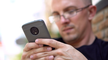 Only Phone in Focus - Late 20s Caucasian Man Texting Using Modern Smartphone With Dual Camera 