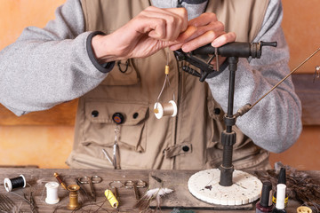 Man making trout flies. Fly tying equipment and material for fly fishing preparation .