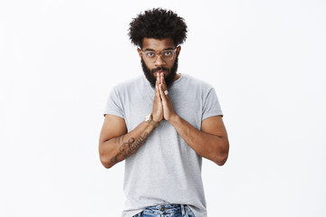 Student bowing to sensei. Portrait of devoted and serious-looking calm african american adult bearded guy in glasses with tattoos and piercing nodding making namaste greeting with hands together
