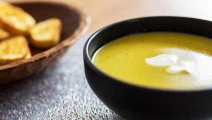 Green broccoli & spinach vegetable soup in black plate on wooden table. Modern kitchen, cooking & healthy food concept. 