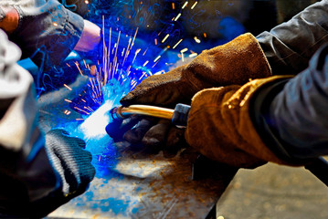 A welder in protective gloves produces a metal connection by electrical welding.
