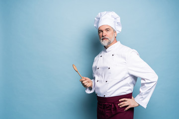 Confident chef. Portrait of mature chef with wooden spoon isolated on blue.