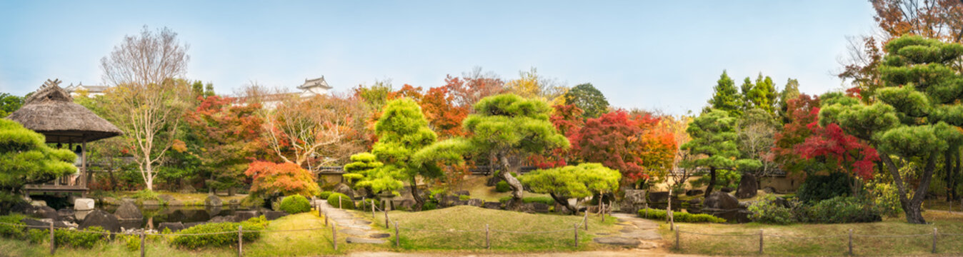 Chinese style garden panorama in autumn at Koko-en Japanese Gardens with small stone bridges over the creek and with the rooftop of Himeji Castle in the background, in Japan.