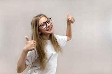 Portrait of a blonde girl with glasses that shows thumbs up. Sign of approval and consent