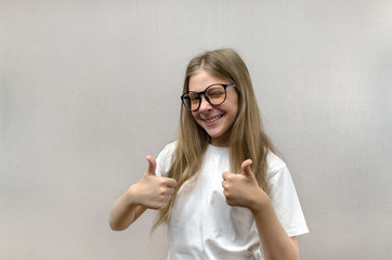Portrait of a blonde girl with glasses that shows thumbs up. Sign of approval and consent