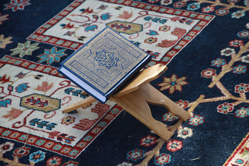 pięknie oprawiony koran leżacy na pulpicie i dywaniku modlitewnym