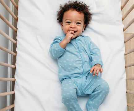 Overhead view of a happy baby boy lying in a crib wearing pajamas