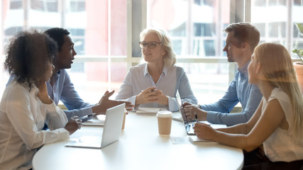 Multicultural professional team colleagues having conversation sit at conference table