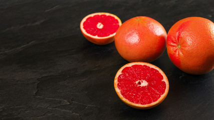 Pink red grapefruits, one citrus halved, on black slate like board, wide photo with empty space for text left side