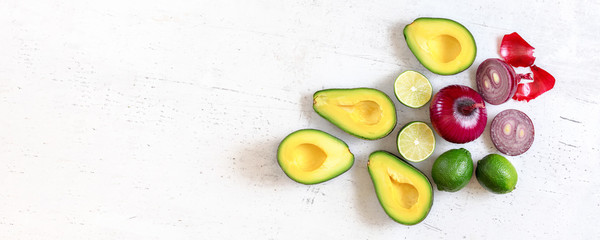 Avocado halves, limes and onions - basic guacamole ingredients on white working board, flat lay photo, wide banner with space for text left side