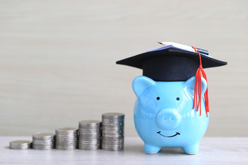 Graduation hat on blue piggy bank with stack of coins money on wooden background, Saving money for education concept