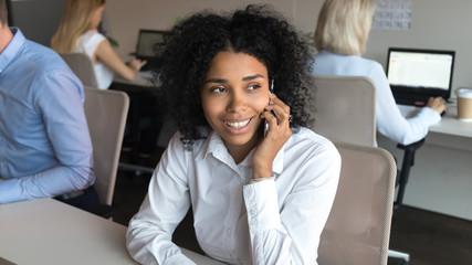 Obraz premium Smiling african american employee talking on phone sitting in office
