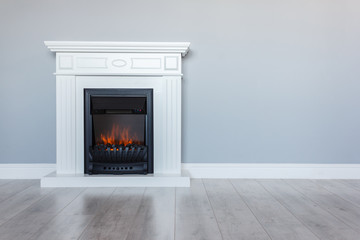 White wooden decorative electric fireplace with a beautiful burning flame. Interior photo on gray background. Place for a simple text. - obrazy, fototapety, plakaty