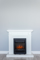 White wooden decorative electric fireplace with a beautiful burning flame. Interior photo on gray background. Place for a simple text. - 261520541