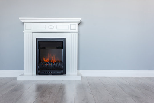 White wooden decorative electric fireplace with a beautiful burning flame. Interior photo on gray background. Place for a simple text.