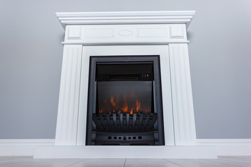 White wooden decorative electric fireplace with a beautiful burning flame. Interior photo on gray background.