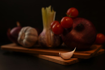 Vegetable set for meat, sauce or salad on a dark background. Garlic clove in the foreground. Garlic, onions and tomatoes are on the cutting board in the back. Healthy food.