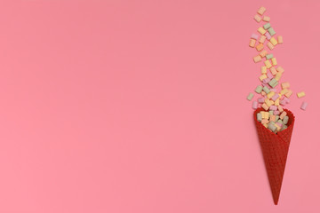 Red waffle ice cream cone. The lie about multi-colored marshmallows isolated on a pink background. Congratulations, celebration concept. Top view. Copy space.