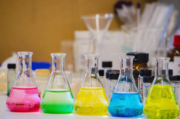 Multiple colorful solution in conical flask lined on a bench in a chemistry lab with blur...