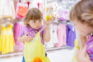 Adorable smiling little girl at the clothes store, try on new yellow summer dress