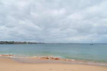 Fototapeta na wymiar Sandy ocean beach with soft waves and yachts in the lagoon