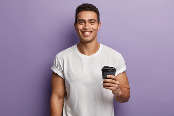 Waist up shot of smiling cheerful handsome guy holds paper takeaway coffee, enjoys spare time with...