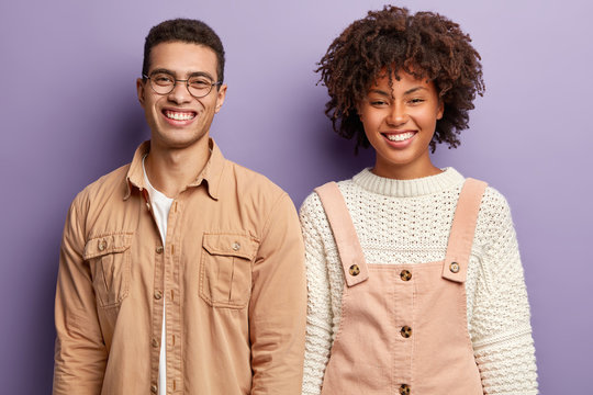 Positive diverse students have broad smiles, express good emootions, stand closely, happy to finish home assigment, wear fashionable clothes, isolated over purple studio wall. Emotions concept - Powered by Adobe