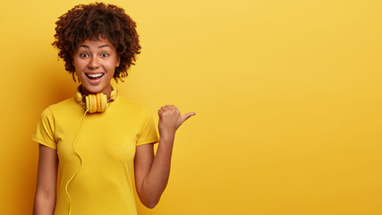 Isolated shot of happy Afro American woman has curly hair, glad facial expression, points with...