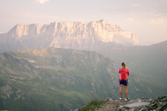 A hiker enjoying the view of sunsrise over the mountains and valleys of the Alps in summer.