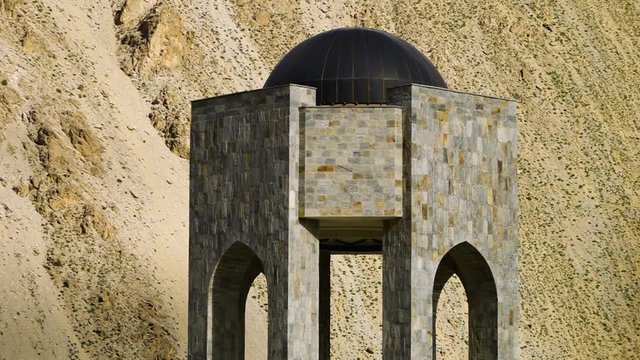 A steady, close up shot of a mosaic tower placed in front of a hill of sand.