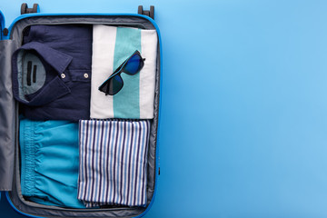 Travel suitcase with clothes on blue background