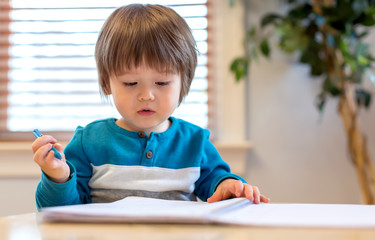 Toddler boy drawing with pen and paper at his desk