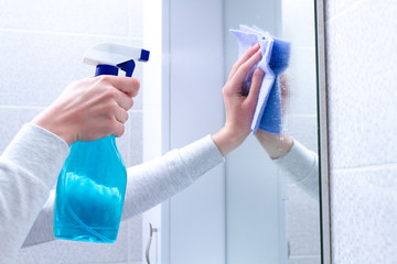 Cleaning and polish mirror with rag and spray in bathroom at home. Housekeeping and cleaning...