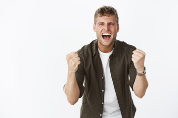 Come on you can do it. Portrait of active and energized supportive boyfriend with fair hair yelling at you with clenched fists in joy and cheer, trying boost confidence standing excited over gray wall